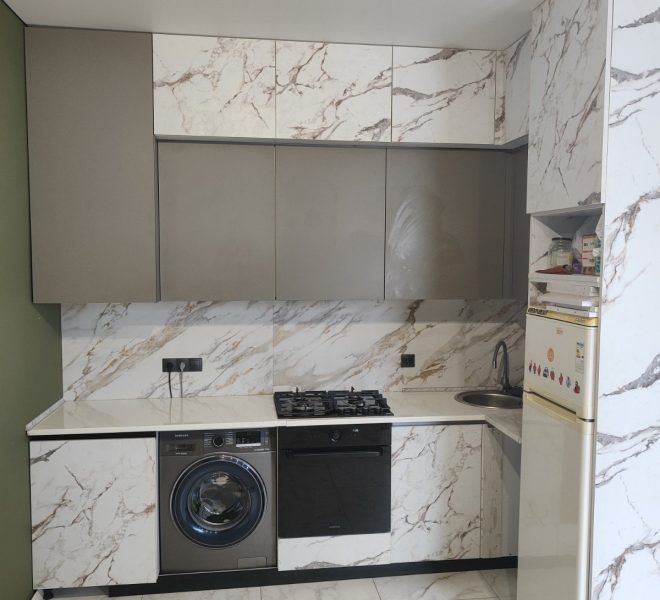 Modern kitchen with marble-pattern cabinets, grey upper doors, and built-in oven, stove, washing machine, and a tall fridge on the right.